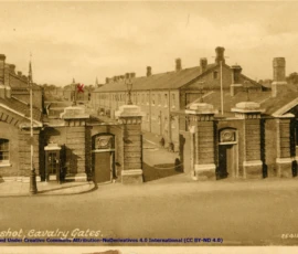 Artifact 1940-08-01-a - Postcard of Warburg Barracks Calvary Gates, sent from Aldershot, England, United Kingdom - Postcard, Obverse.Annotation:
"Entrance to our barracks. The red cross (x) on the end of one building indicates the building We're in."